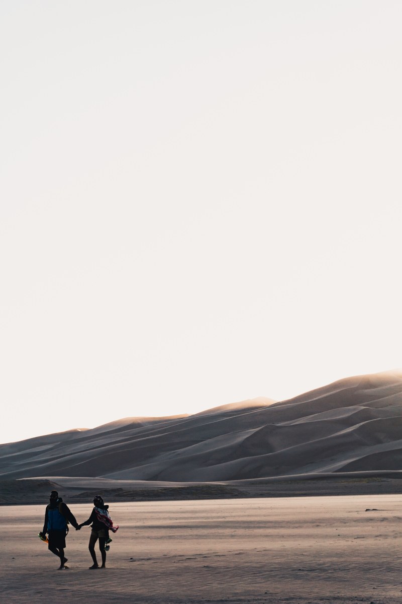 couple holding hands walking through great sand dunes national park and preserve during sunset, just leaving 4k