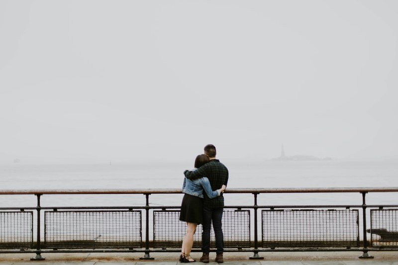 a couple holds one another on a pier overlooking a body of water and overcast sky, hold me 4k