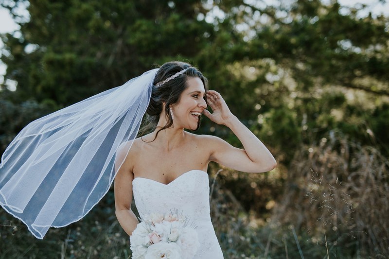 bride stands in front of trees laughing as the wind blows her veil, laughing bride with blowing veil 4k