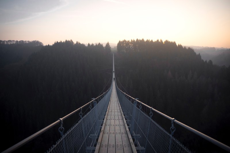 a distant shot of two people on a long suspension bridge with metal rails, long suspension bridge 4k