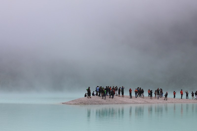 diverse group of tourists stand on a peninsula on a foggy day, sightseeing on the beach 4k