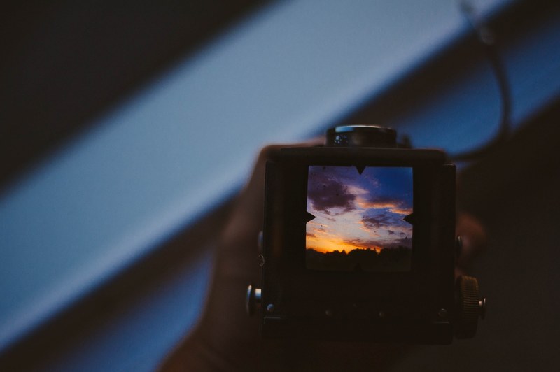 a view from behind a vintage camera toward the viewfinder that displays a yellow and blue sunset sky, reviewing photography 4k