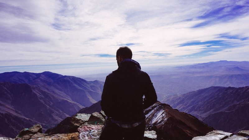 a man standing on top of a mountain viewing his hiking path down, man on top of mountain 4k