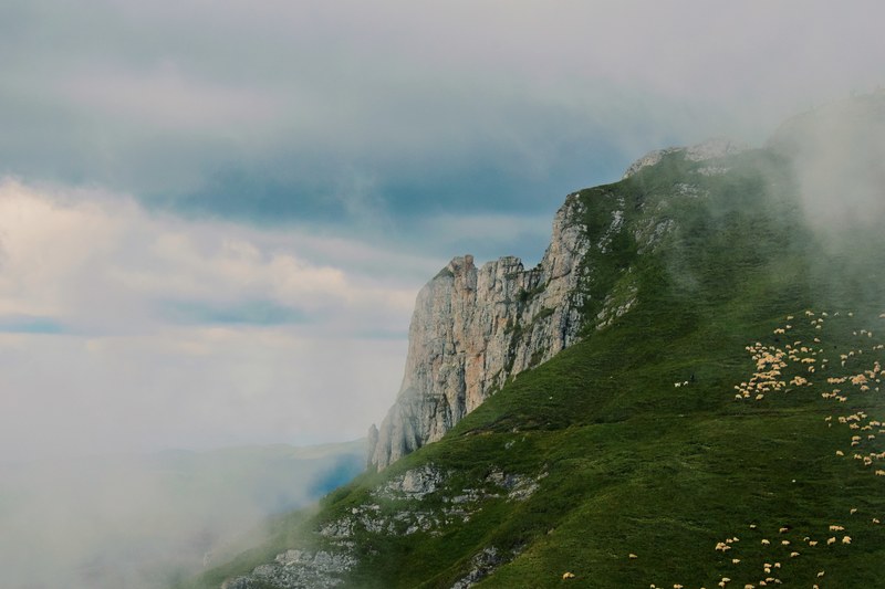 clouds cover a rocky ridge surrounded by green pastures, clouds and cliffs 4k