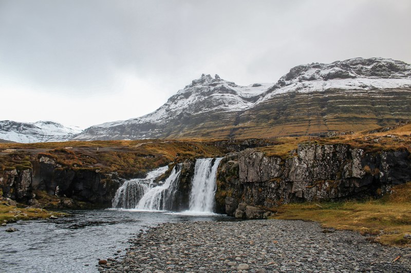 a waterfall pouring down from a rocky plateau with steep mountains at the back, waterfall in iceland 4k