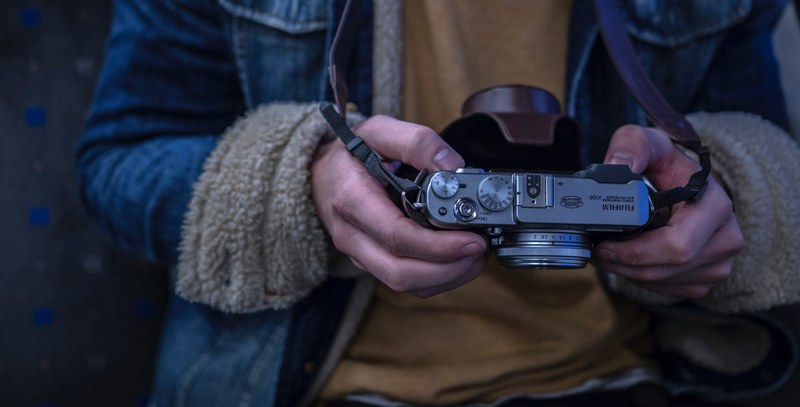 a person wearing a shearling coat holding a fujifilm camera in their hands, denim jacket camera strap 4k