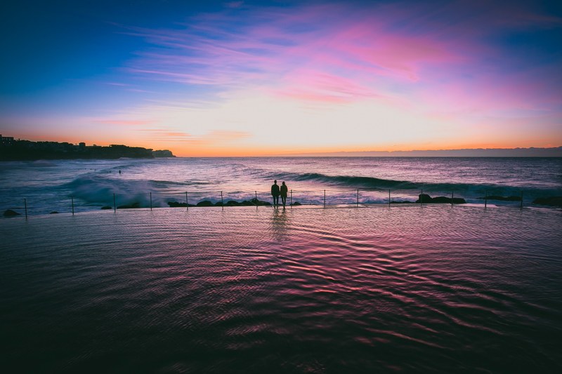 couple holding hands at sunset on the edge of infinity pool by the ocean at bronte beach, couple at sunset by the ocean 4k