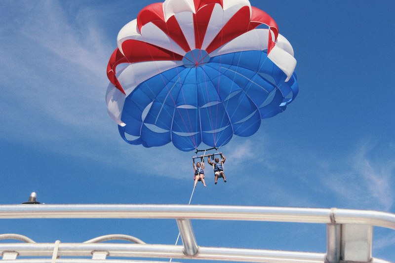 people parasail with a parachute behind a boat on a bright blue day, parasailing in the bahamas 4k