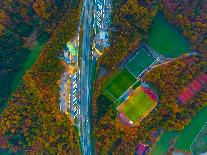 a colorful aerial shot of a highway running next to soccer pitches with light reflecting off buildings, light reflections by the highway 4k
