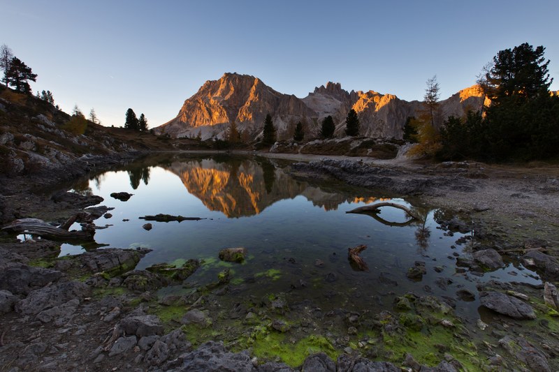 a sunlit rock formation overlooking a small rocky pond, shallow pond at dusk 4k