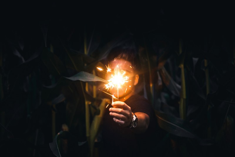 person with watch holds lit sparkler in front of face in the dark, holding sparkler in the dark 4k