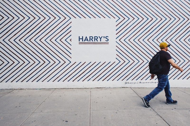 man in hat walks in front of wall with zig zag pattern and a quotharrysquot sign, man walks by harrys sign 4k