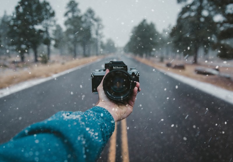 a nikon camera is held facing the photographer standing on an empty road in the snow, _long road nikon 4k