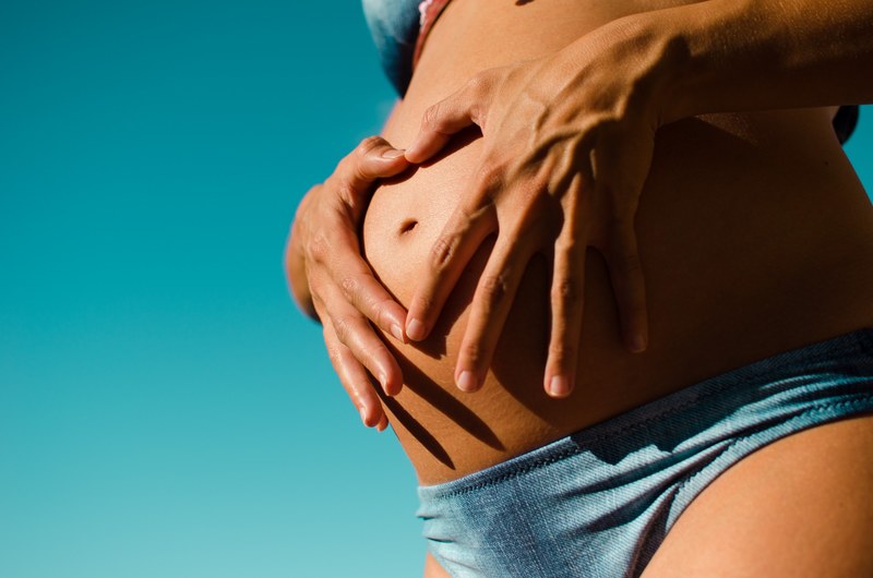 a woman in bikini makes a heart with her fingers placing them over her pregnant belly, pregnancy 4k