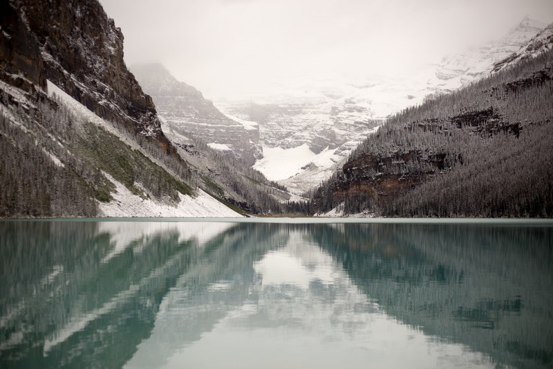 view from the clear surface of a mountain lake on a steep granite face covered in snow, lake louise 4k