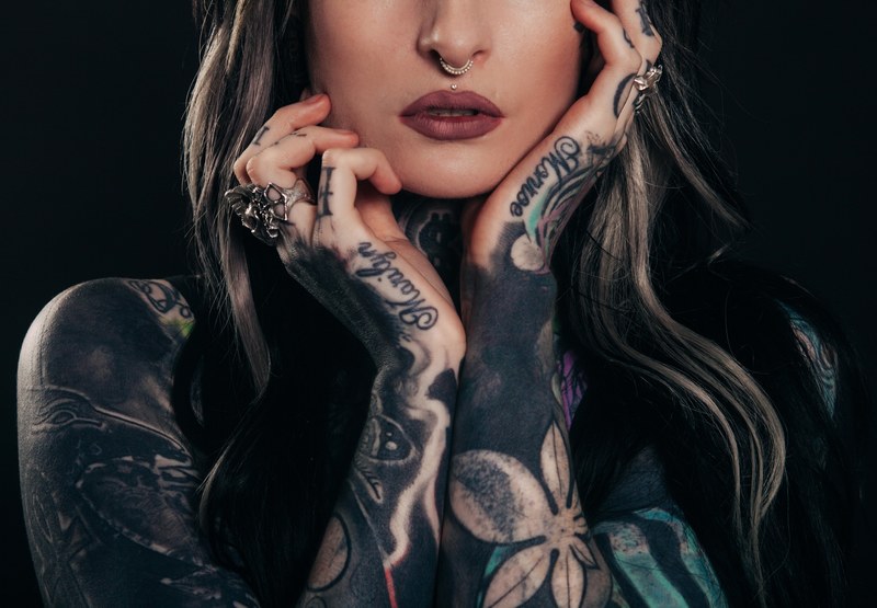 edgy woman with tattoos and a piercing holds her hands against her face, edgy tattoos 4k