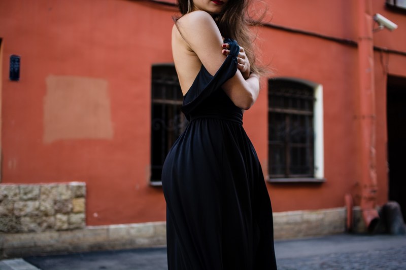 fashionable woman in a chic black dress poses in an alley, little black dress 4k