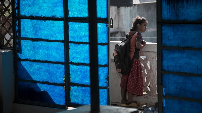 a girl dressed for school peers over the balcony outside of her home, _a girl on a balcony 4k
