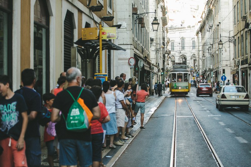 people lining up on the sidewalk as a trolley car approaches the stop, waiting at the trolley stop 4k