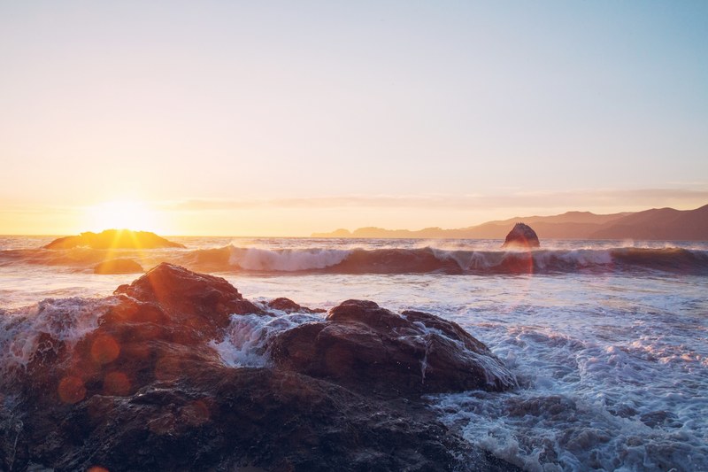 white sea waves hitting against rocks near the shore during sunset, sea foam on rocks at sunset 4k