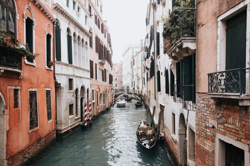 a canal in venice with a gondola in front and a bridge in the back, canal in venice 4k