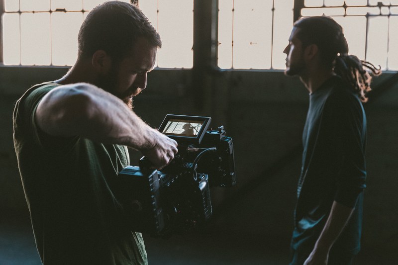 a man with a professional video camera recording another man in an old building, bts 4k