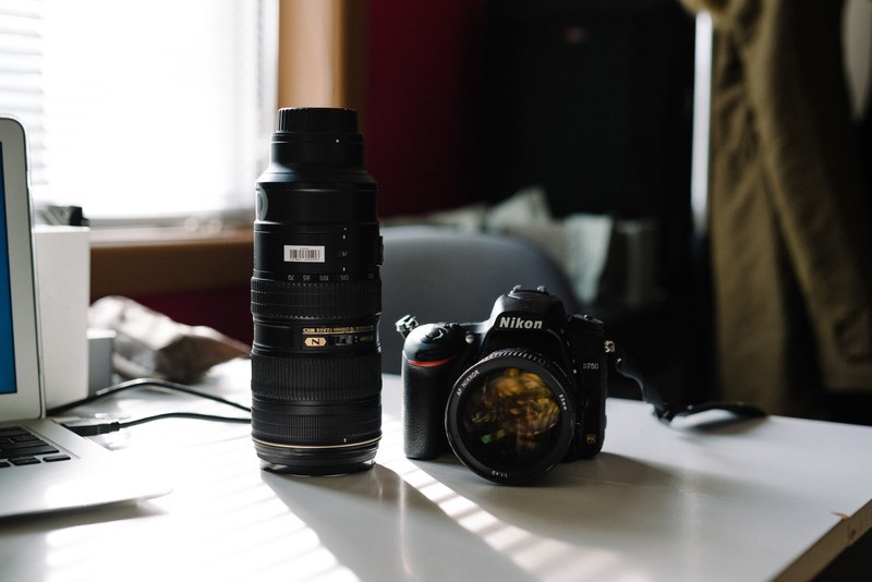 nikon camera with telephoto lens on a table next to a laptop computer, nikon camera telephoto lens 4k