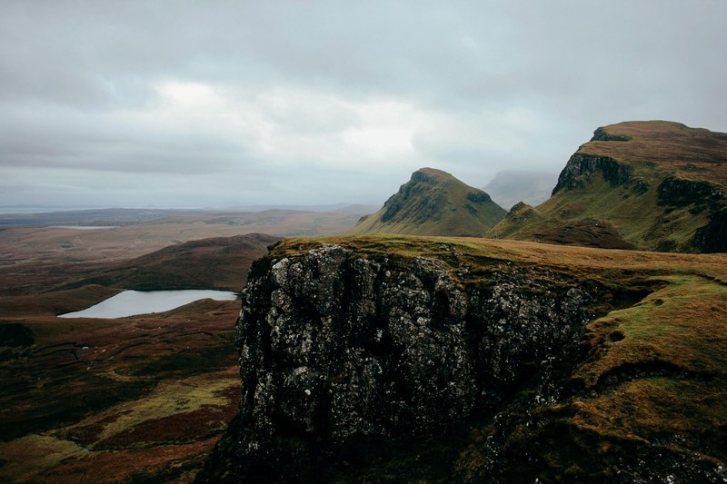 view of a cliff overlooking mountains a lake overcast skies and brown grass, cliff edge and clouds 4k