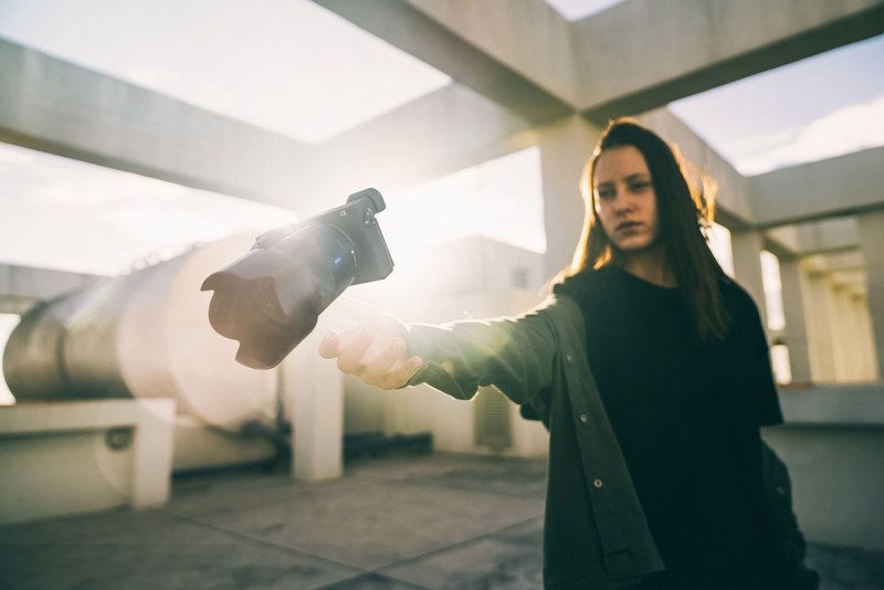 a woman holds out her hand to toss or catch her camera aside concrete pillars, woman catching a camera 4k