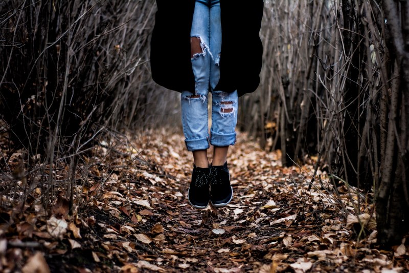 a person in ripped jeans jumping up on a carpet of autumn leaves in a thicket, over a leaf covered path 4k