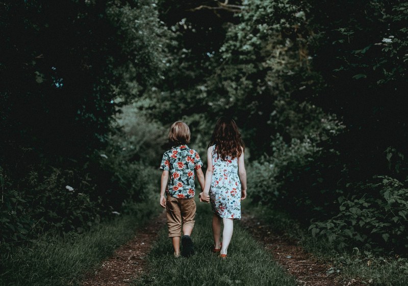 a girl and a boy hold hands and walk down a wooded trail, siblings walking holding hands 4k