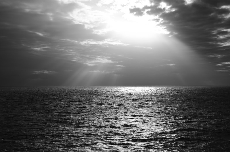 black and white shot of sea with cloudy sky and sunrays coming through clouds, monochrome sunrays and sea 4k
