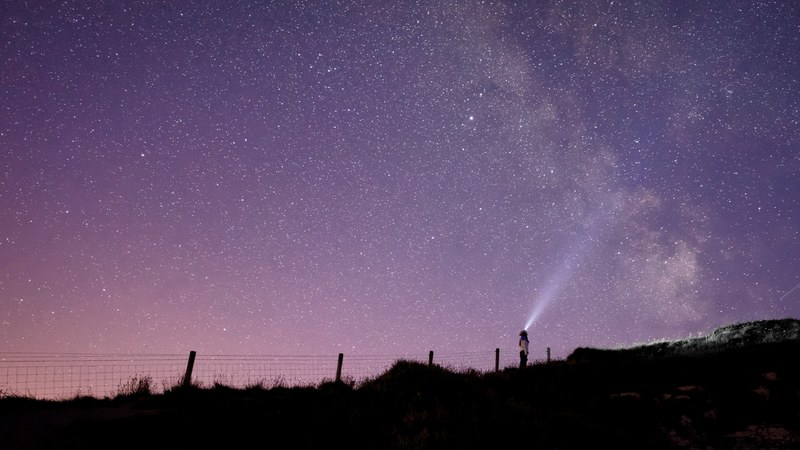 a woman standing in a field at night under a purple sky that shows the milky way at the cliffs of moher, cliffs of moher milky way 4k