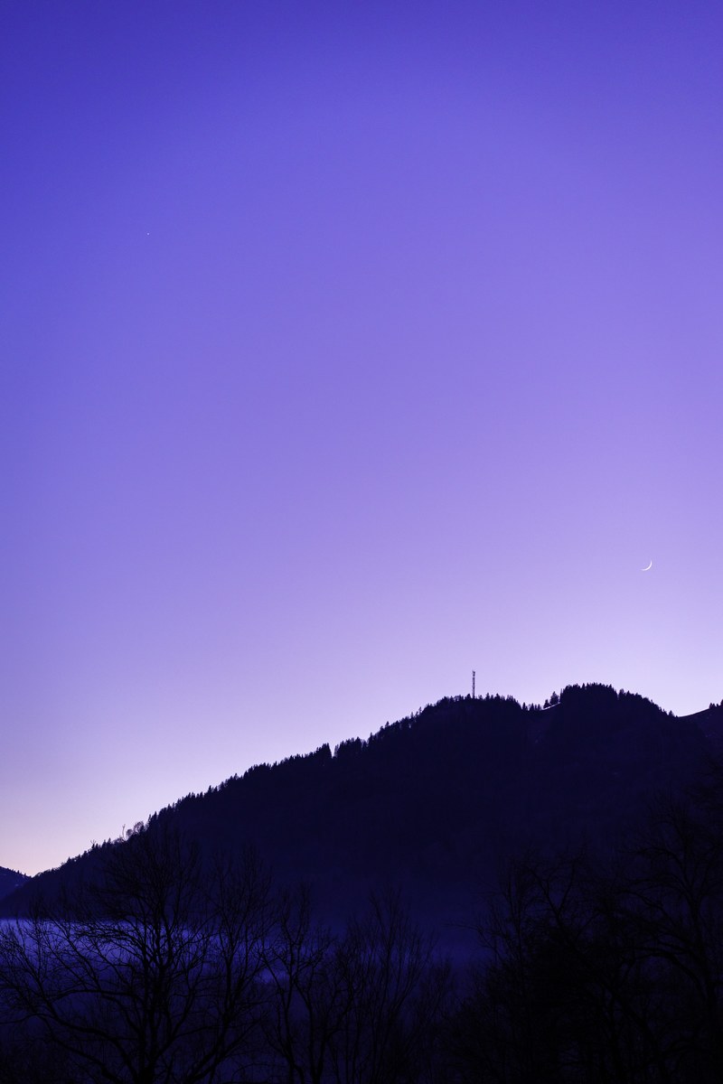 a crescent moon hangs low above the hills silhouetted against a purple sky, moon in the blue sky 4k