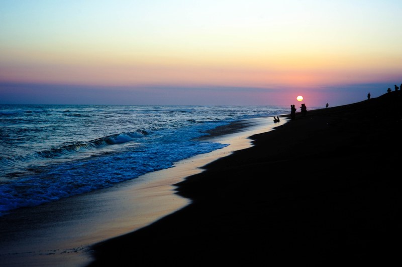 silhouetted people on the beach as the waves lap the shore while the sun sets over the coast, sunset over the beach 4k