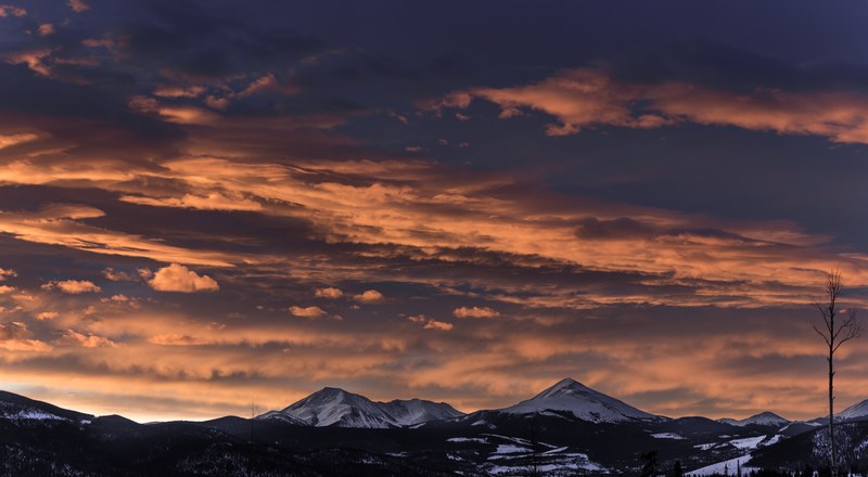 snowcap mountain range horizon view at silverthorne and large sun tinged clouds in sky and single tree in foreground, snowcap mountain range and large clouded sky 4k