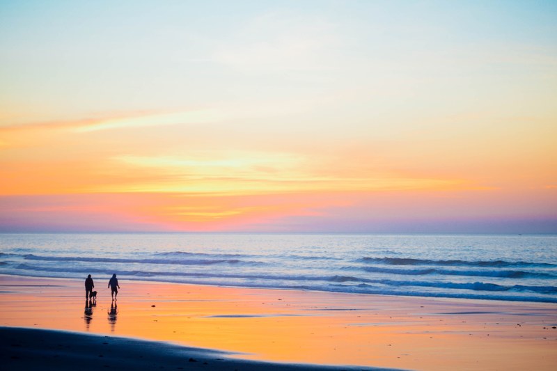 a family by the moody beach ocean watching the orange and blue sunset, family watching beach sunset 4k