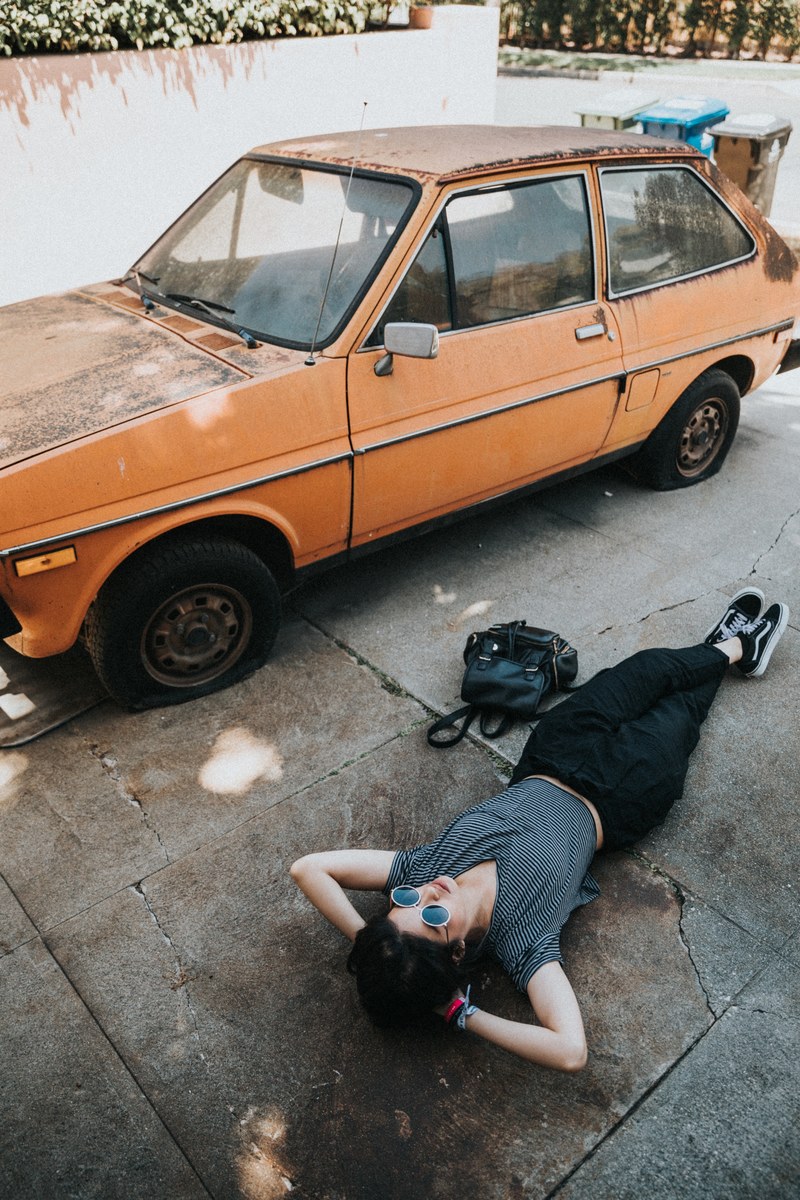 a woman lying down next to an old orange car, _lying near orange car 4k