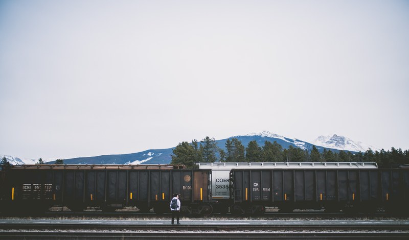 person alone with backpack standing near cargo train and railroad in jasper, cargo train and person in jasper 4k
