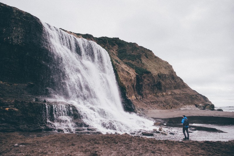 a male hiker standing near a small waterfall, in awe 4k