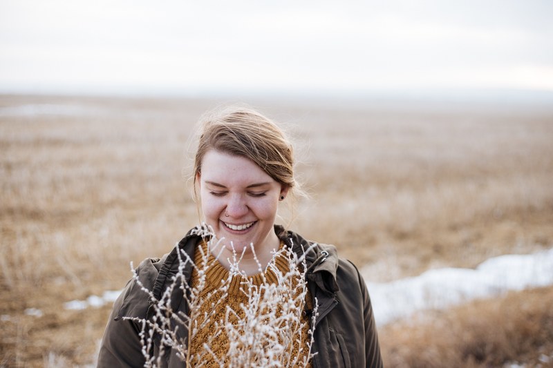 a woman in a coat smiles with closed eyes in a brown field, closed eye smile in field 4k