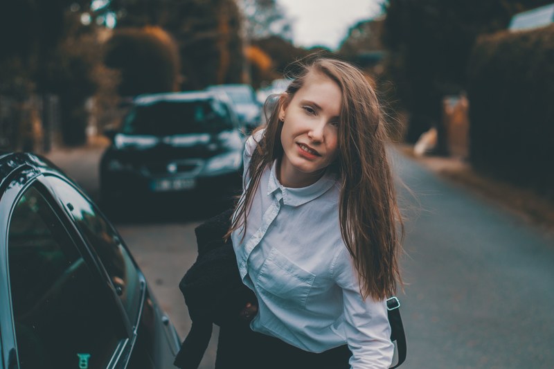 woman with long hair in buttoned up blue shirt leaning forward by the car in the streets of hamburg, woman leaning by the car in hamburg 4k