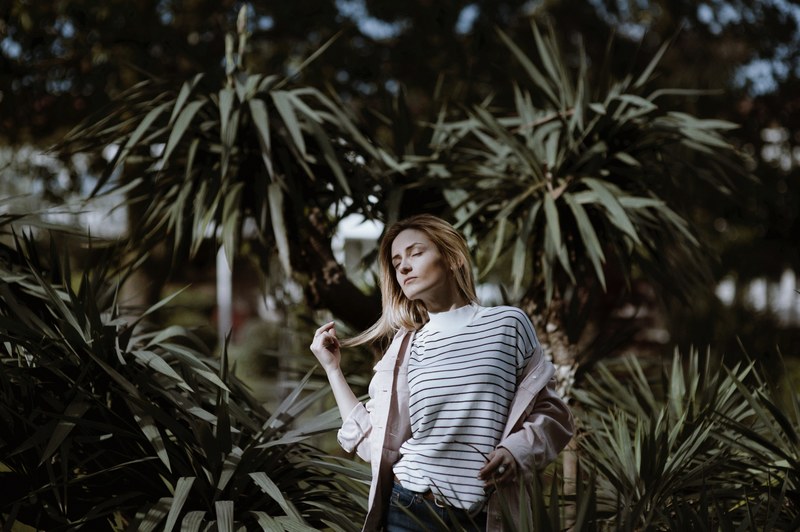a blonde woman plays with her hair while closing her eyes before green plants in batumi, feel nature 4k