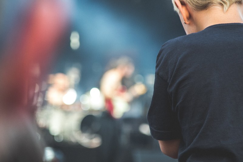 standing behind a person with a blurry band playing on stage in the background, band photographer 4k