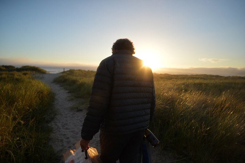 a person in shadow faces away toward a sunset over the ocean in manzanita, person facing ocean sunset 4k