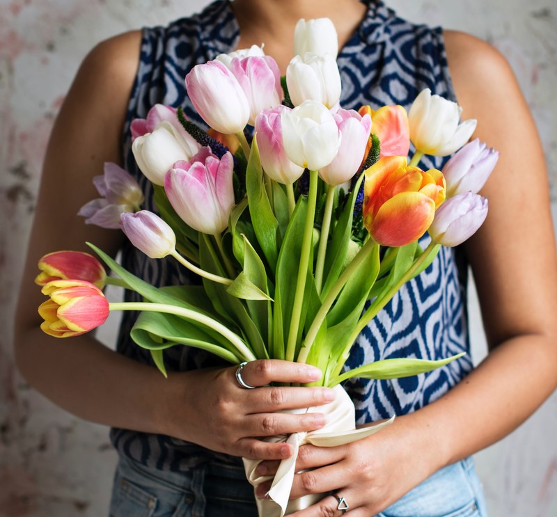 a woman holding a large bouquet of tulips in front of her chest, presenting a floral bouquet 4k