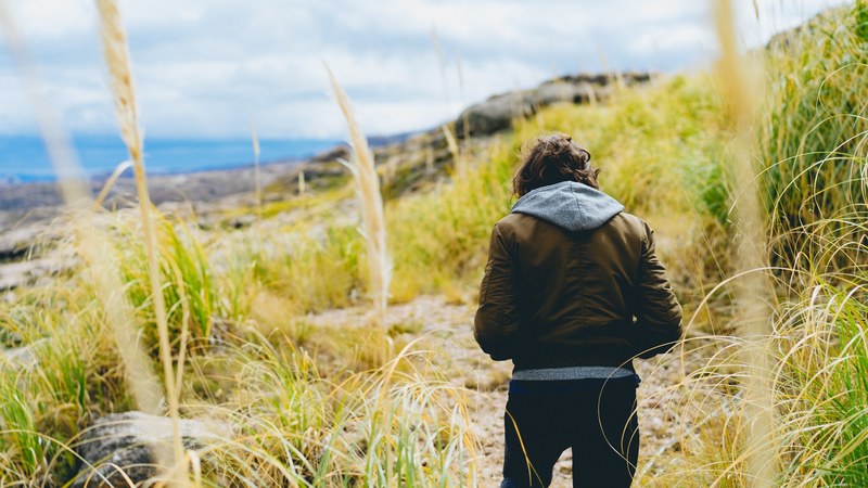 person in a brown leather jacket and gray hoodie in field of wheat beside the sea, person in wheat field by sea 4k