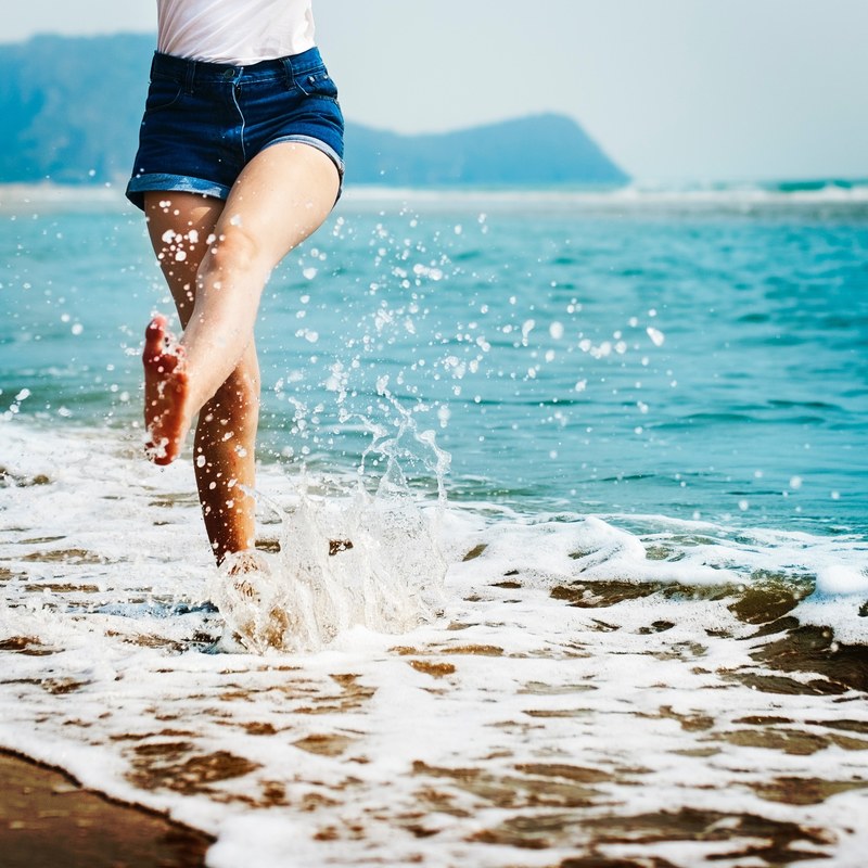 a girl wearing jean shorts splashing her feet in the ocean, ocean splashing 4k