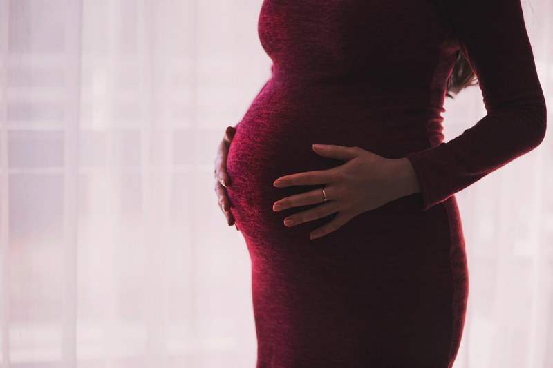 pregnant woman in form fitting crimson dress holds belly, any day now 4k