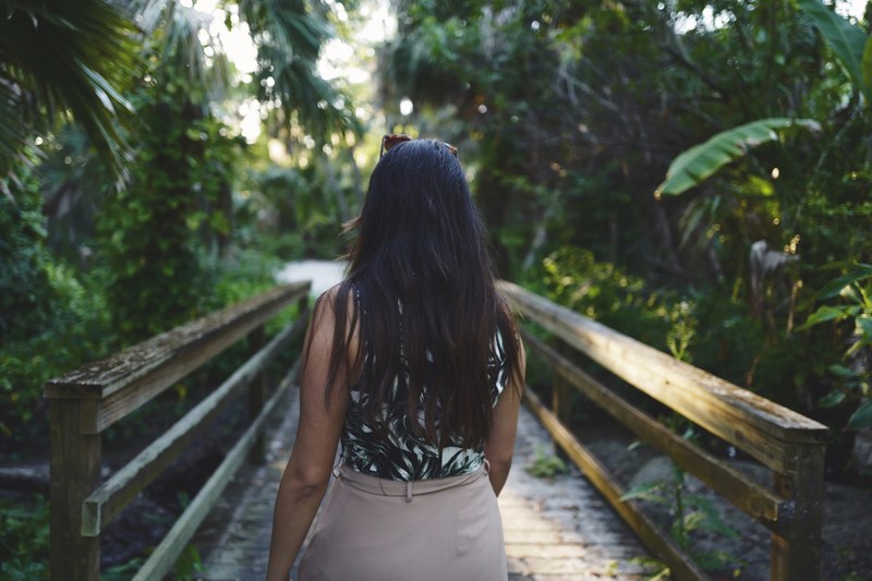 a dark haired woman walking across a small bridge in a tropical setting, bridge through the rainforest 4k